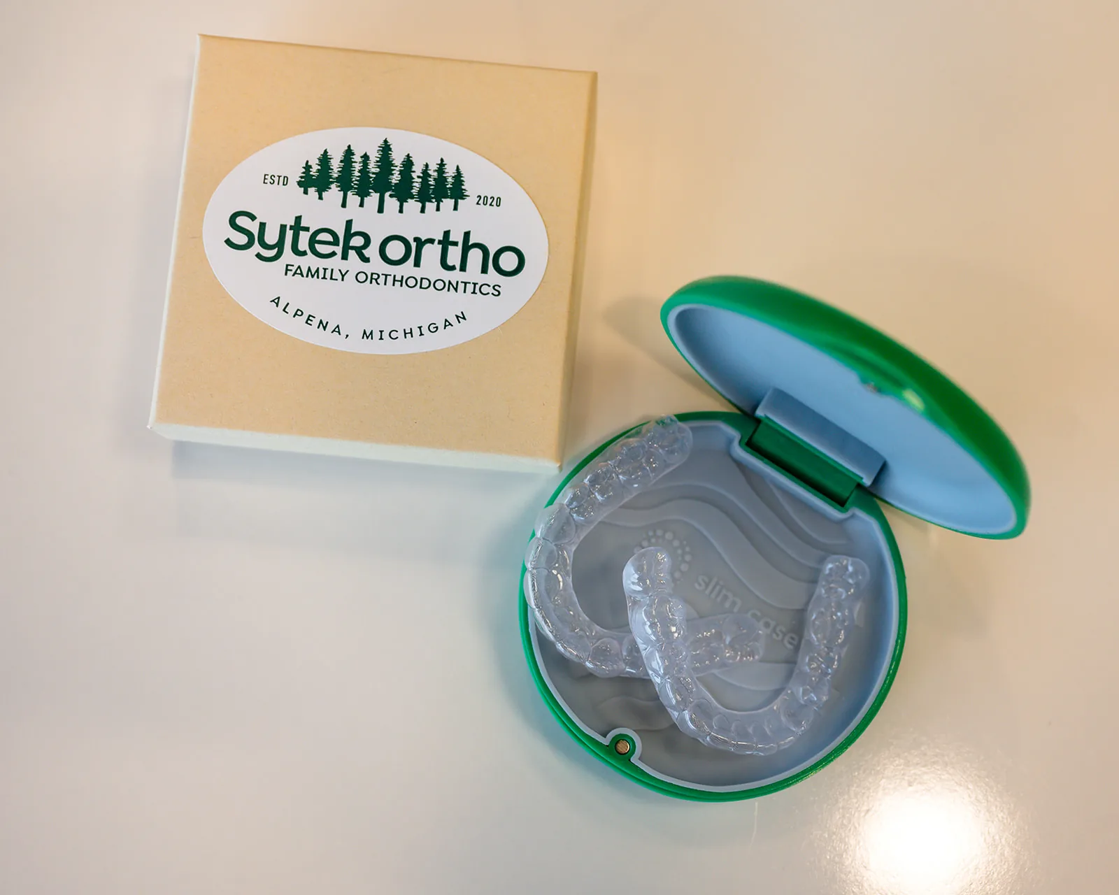 A clear Sytek Ortho retainer in its branded case beside the practice gift box